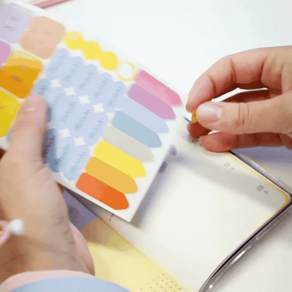Manos despegando stickers de colores de la plancha incluida en la agenda Happimess Astro