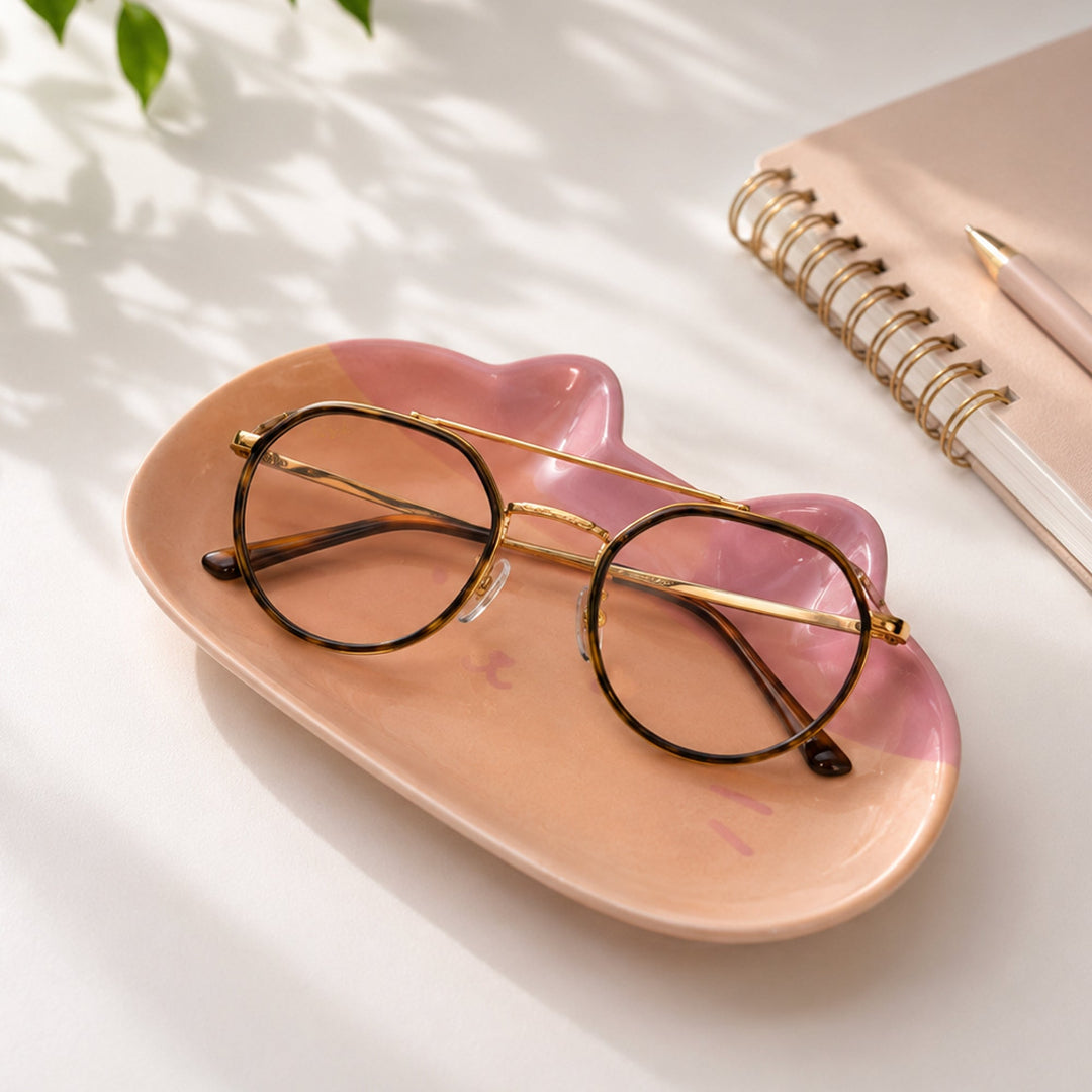 Bandeja con forma de cara de gato rosa y naranja encima de una mesa de escritorio con unas gafas encima