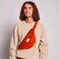 Chico con pelo largo rizado con una riñonera de pana de color rojo ladrillo de la marca francesa Hindbag