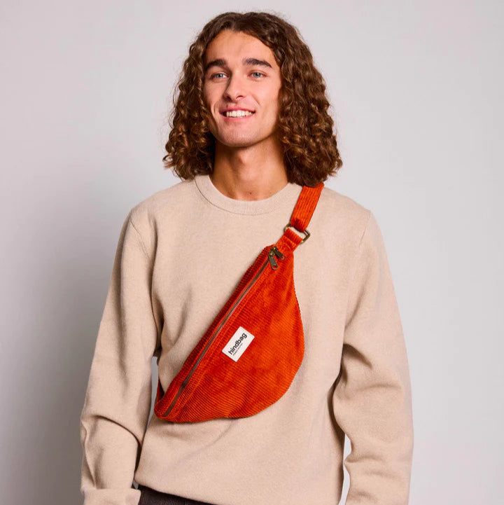Chico con pelo largo rizado con una riñonera de pana de color rojo ladrillo de la marca francesa Hindbag