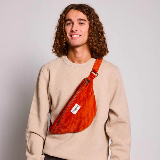 Chico con pelo largo rizado con una riñonera de pana de color rojo ladrillo de la marca francesa Hindbag