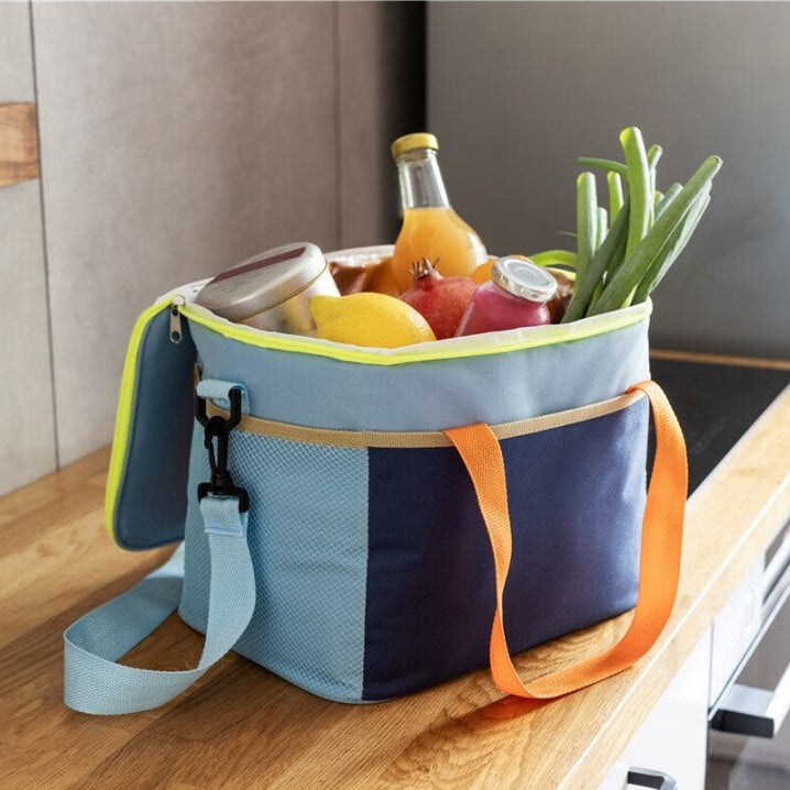 Bolsa térmica Nick de la marca Remember en tonos azules con detalles naranjas y amarillos rellena de diferentes verduras y bebidas. 