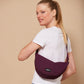 Mujer rubia con camiseta blanca y un bolso riñonera con forma de media luna color ciruela de la marca francesa Hindbag