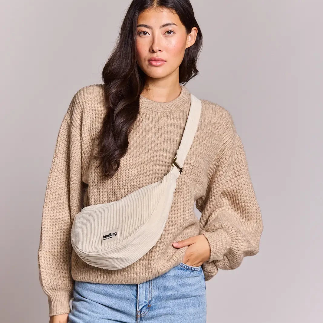 Mujer con un jersey de lana y el bolso riñonera de pana beige de la marca Hindbag con forma de media luna