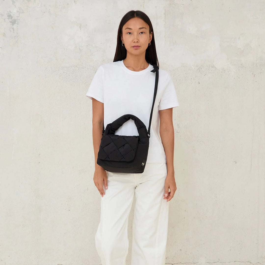 Modelo de frente con el mini bolso acolchado Ani de Lefrik en negro en bandolera combinado con pantalones y camiseta blancos