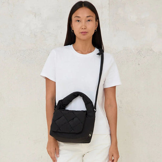 Modelo de frente con el mini bolso acolchado Ani de Lefrik en negro en bandolera combinado con pantalones y camiseta blancos