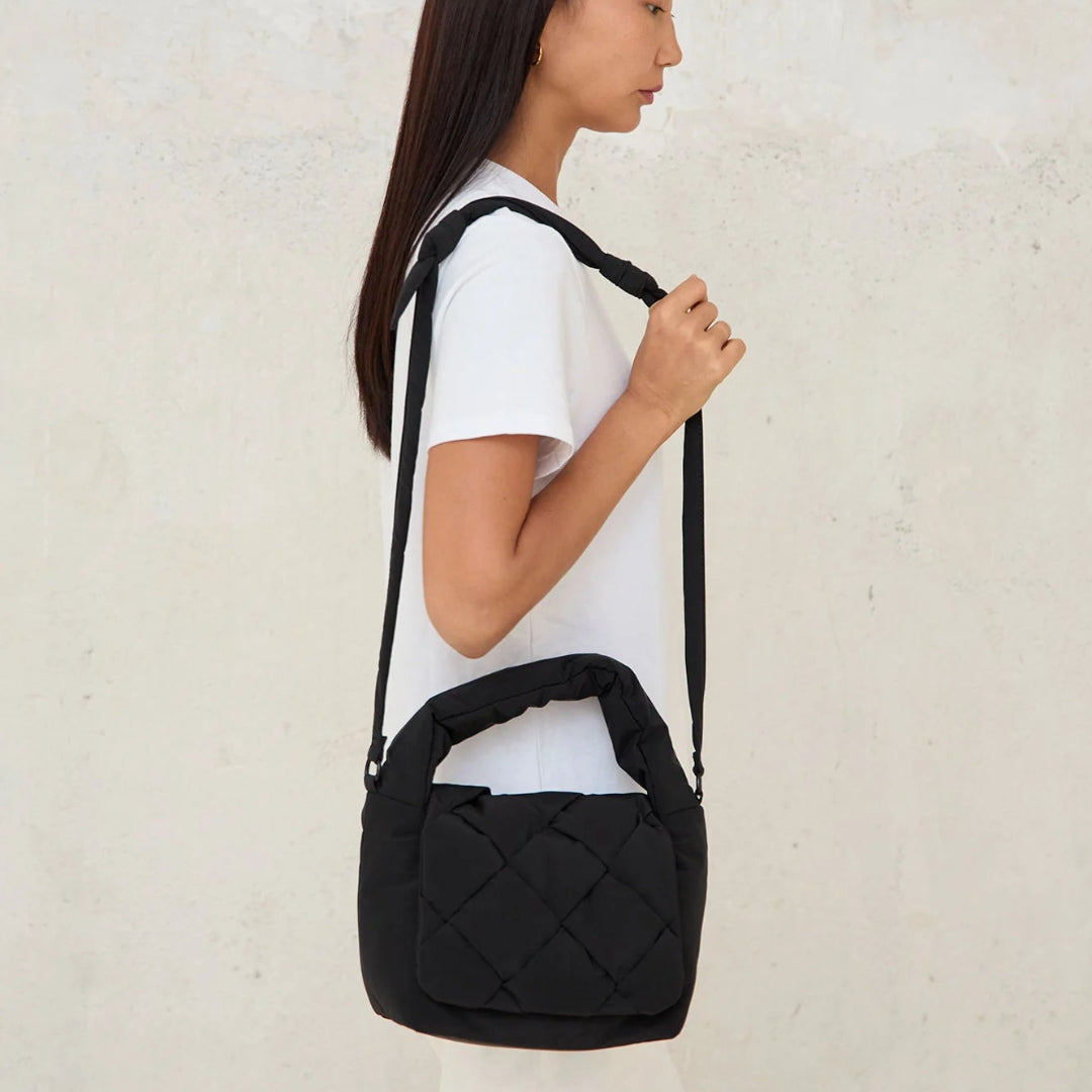 Modelo de perfil con el mini bolso acolchado Ani de Lefrik en negro en bandolera, sujetando la correa ajustable