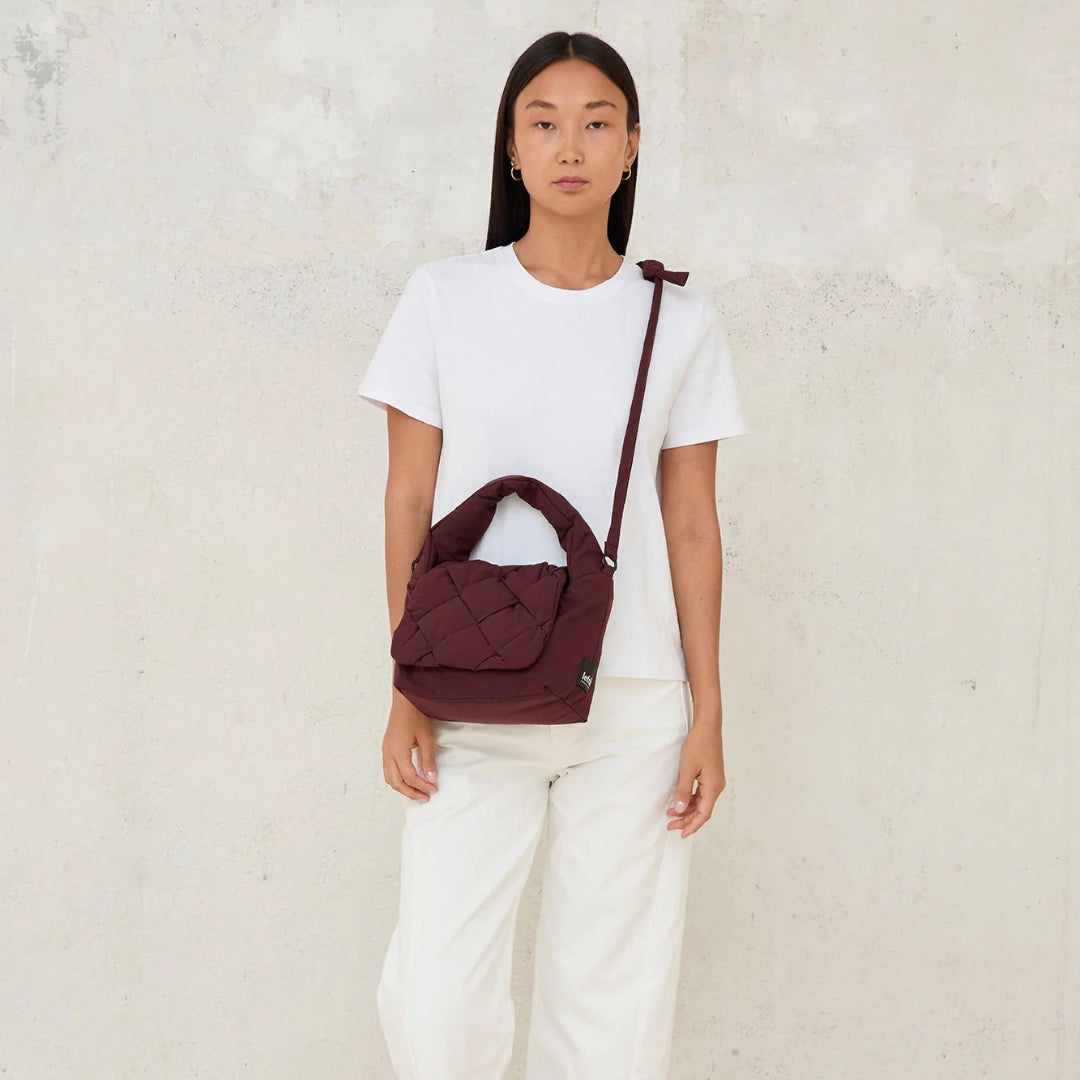 Modelo llevando el mini bolso acolchado Ani de Lefrik en burdeos cruzado al cuerpo, vista frontal completa