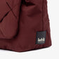 Detalle de la etiqueta Lefrik sobre el tejido acolchado en color burdeos del bolso Ani mini