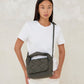 Modelo llevando el bolso Ani mini de Lefrik en verde musgo cruzado al cuerpo, combinado con camiseta blanca y pantalón blanco