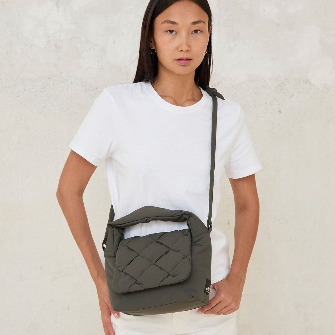 Modelo llevando el bolso Ani mini de Lefrik en verde musgo cruzado al cuerpo, combinado con camiseta blanca y pantalón blanco