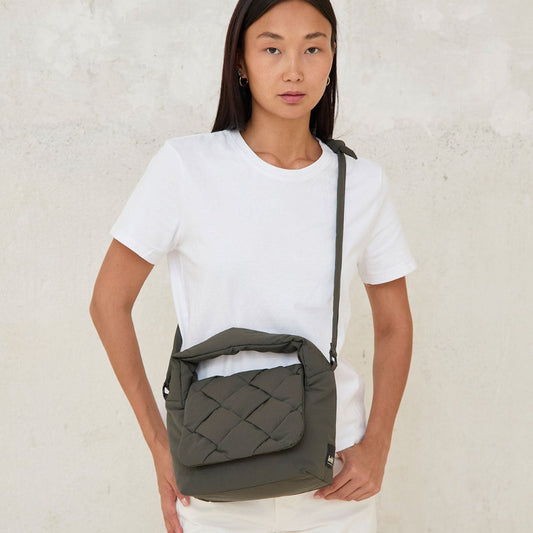 Modelo llevando el bolso Ani mini de Lefrik en verde musgo cruzado al cuerpo, combinado con camiseta blanca y pantalón blanco
