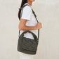 Modelo llevando el bolso Ani mini de Lefrik en verde musgo colgado al hombro, combinado con camiseta blanca y pantalón blanco