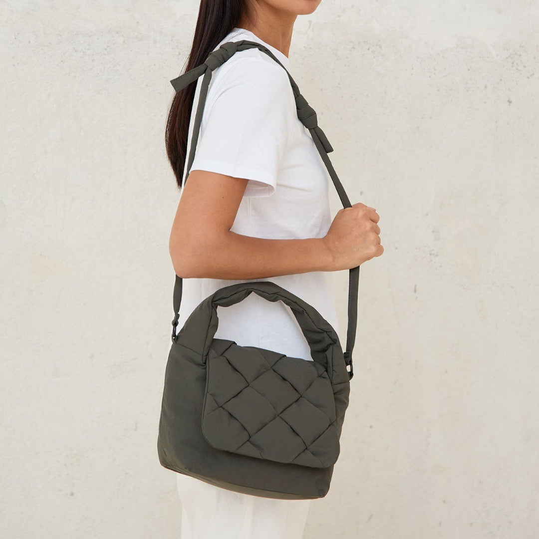 Modelo llevando el bolso Ani mini de Lefrik en verde musgo colgado al hombro, combinado con camiseta blanca y pantalón blanco