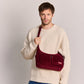 Hombre con jersey blanco y vaqueros con el bolso de pana color burdeos, dos bolsillos frontales con cremallera y correa ajustable de la marca francesa Hindbag 