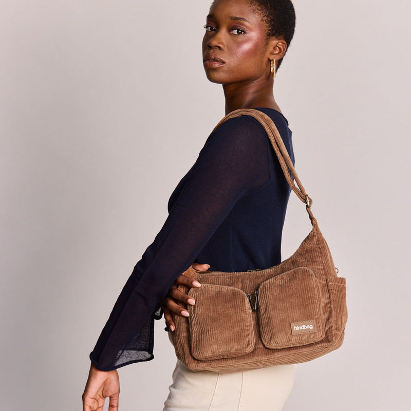Mujer de perfil con bolso de pana color marrón con dos bolsillos frontales con cremallera y correa ajustable de la marca francesa Hindbag 