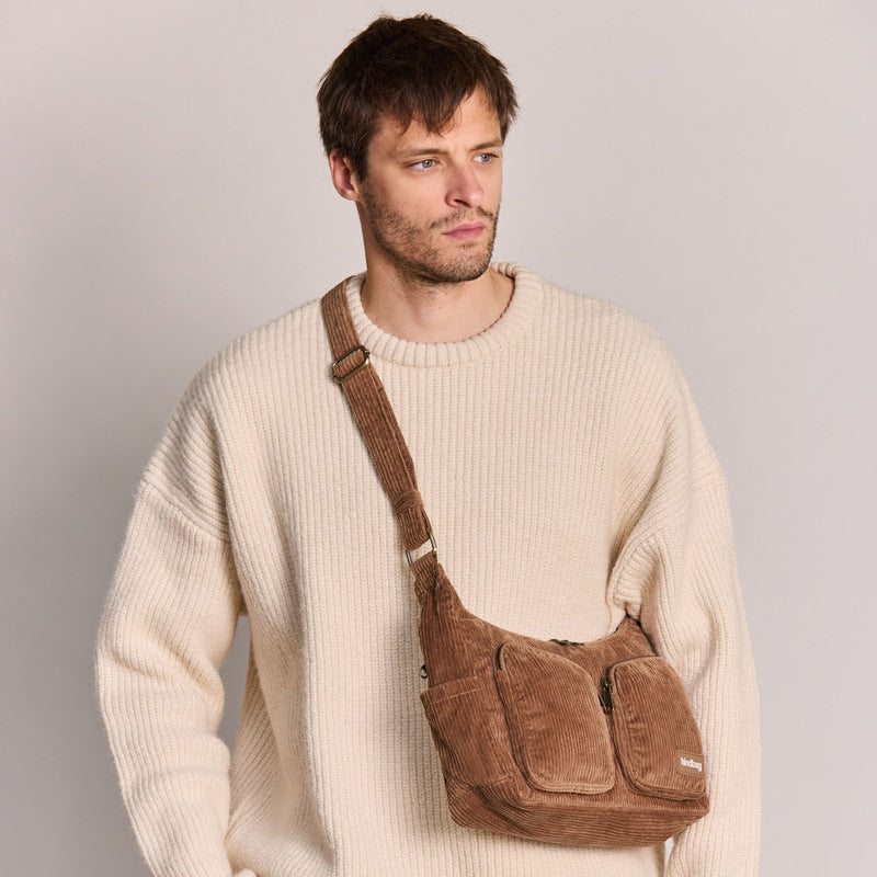 Chico con jersey de canalé blanco y un bolso de pana color marrón con dos bolsillos frontales con cremallera y correa ajustable de la marca francesa Hindbag 
