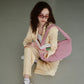 Mujer sentada en el suelo leyendo un libro con traje de chaqueta beige y bolso rosa acolchado de Lefrik