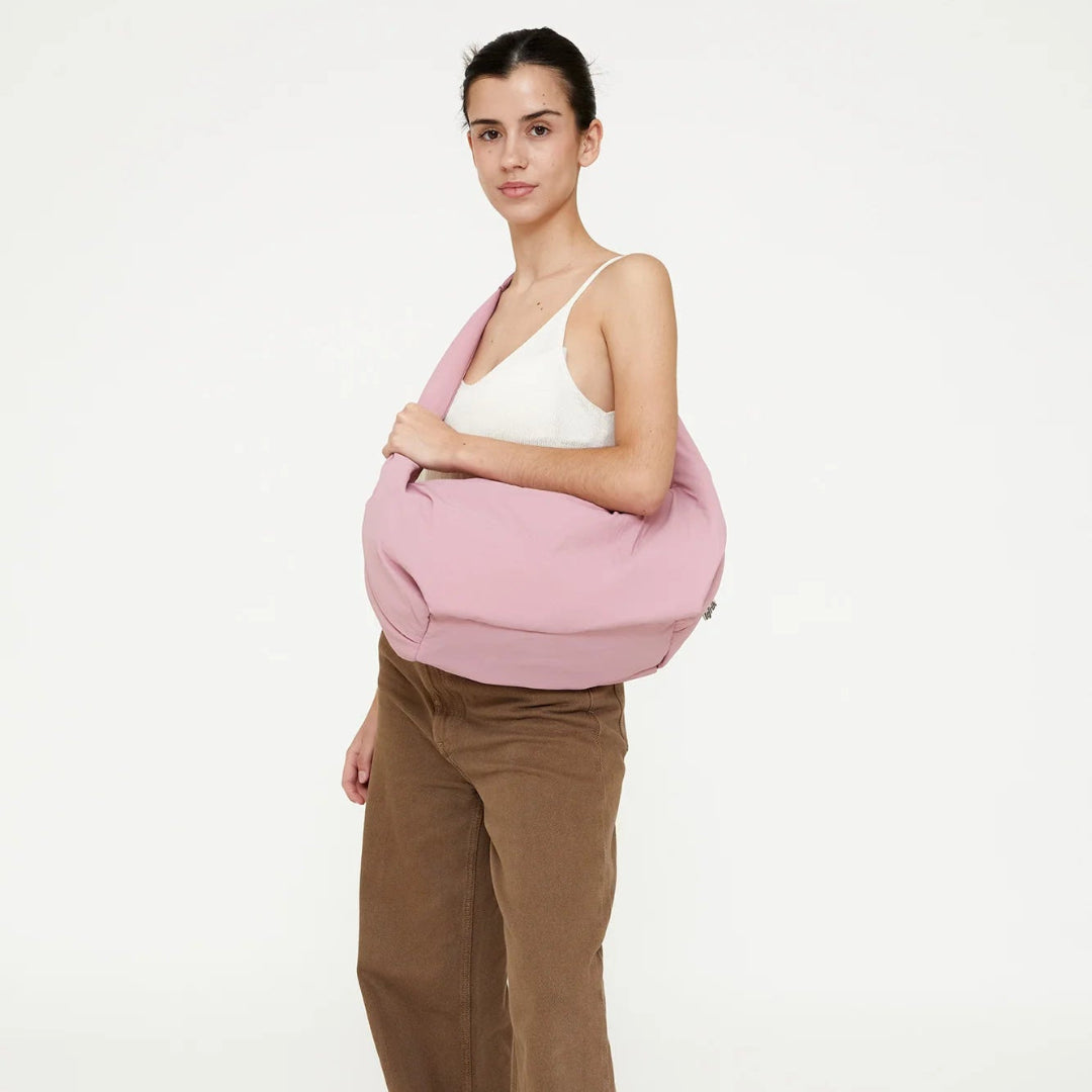 Mujer con pantalón marrón y camiseta blanca llevando el bolso Myra acolchado de color rosa y un asa larga para llevar al hombro de la marca española Lefrik