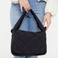 Bolso negro Ani de Lefrik con solapa trenzada y asa acolchada, sostenido de la mano por una modelo con vaqueros.