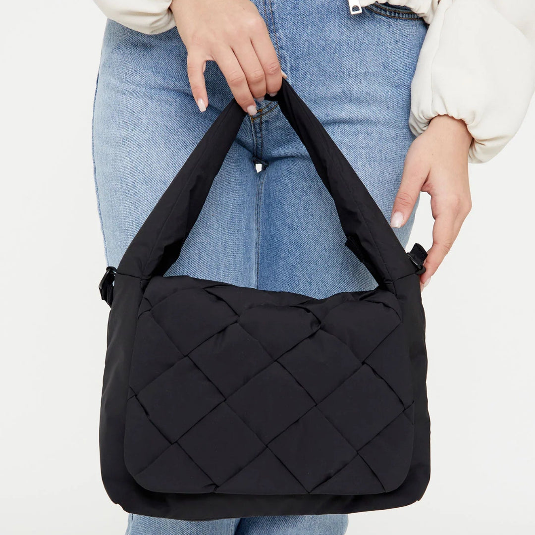Bolso negro Ani de Lefrik con solapa trenzada y asa acolchada, sostenido de la mano por una modelo con vaqueros.