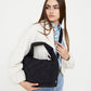Modelo con chaqueta blanca y vaqueros llevando el bolso negro trenzado Ani de Lefrik colgado del hombro.