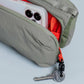 Detalle del bolso Bottle Sacoche Medium Topologie en color caqui con cremallera abierta, móvil en el interior y llave colgando del tirador
