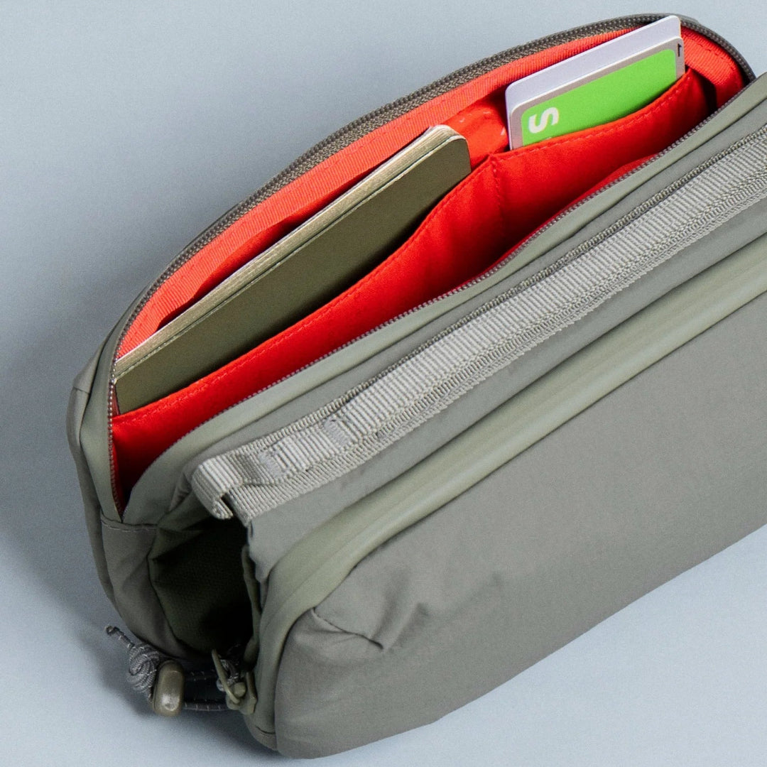 Interior del bolso Bottle Sacoche Medium Topologie en color caqui con forro rojo, compartimento principal abierto con tarjetas y documentos en el interior
