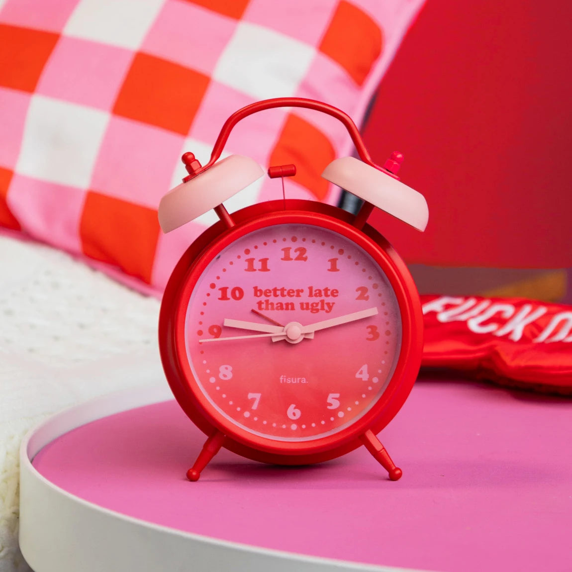 reloj retro con el texto Better late than ugly en colores rojos y rosas, sobre una mesa de una habitación con colores rosas y rojos
