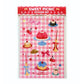 pack de pegatinas con el texto sweet picnic sticker set con una hoja de pegatinas que tiene pasteles con caritas, una tarta de gelatina, candelabros, una taza de café, cerezas, gafas en forma de corazón sobre un fondo a cuadros rosas y blancos imitando un mantel de picnic