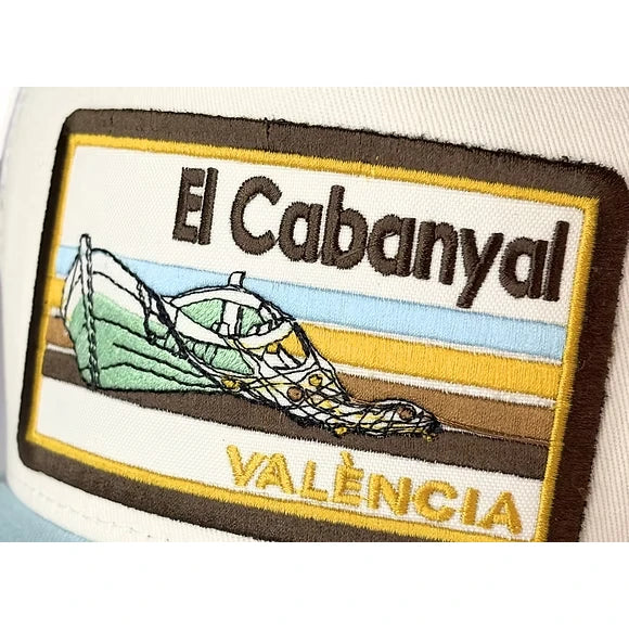 Detalle del parche de la gorra con visera azul claro del barrio del Cabañal en Valencia con el diseño de una barca y redes de pesca en colores azules y marrones