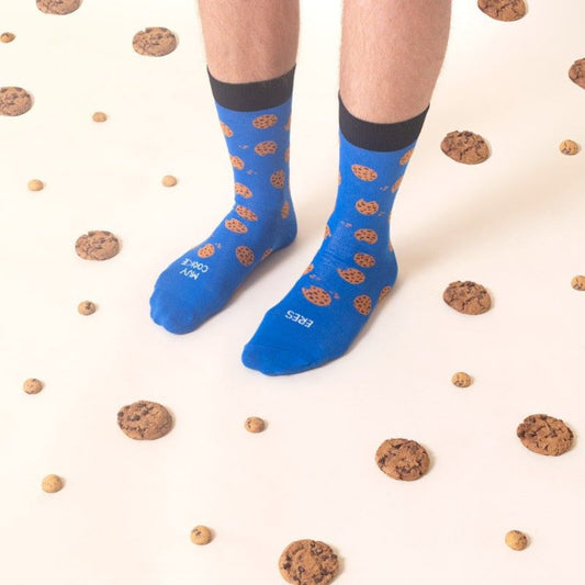 Piernas con los calcetines del color del Monstruo de las Galletas estampados con galletas con pepitas de chocolate y el mensaje Eres muy cookie en un suelo cubierto de galletas con pepitas de chocolate