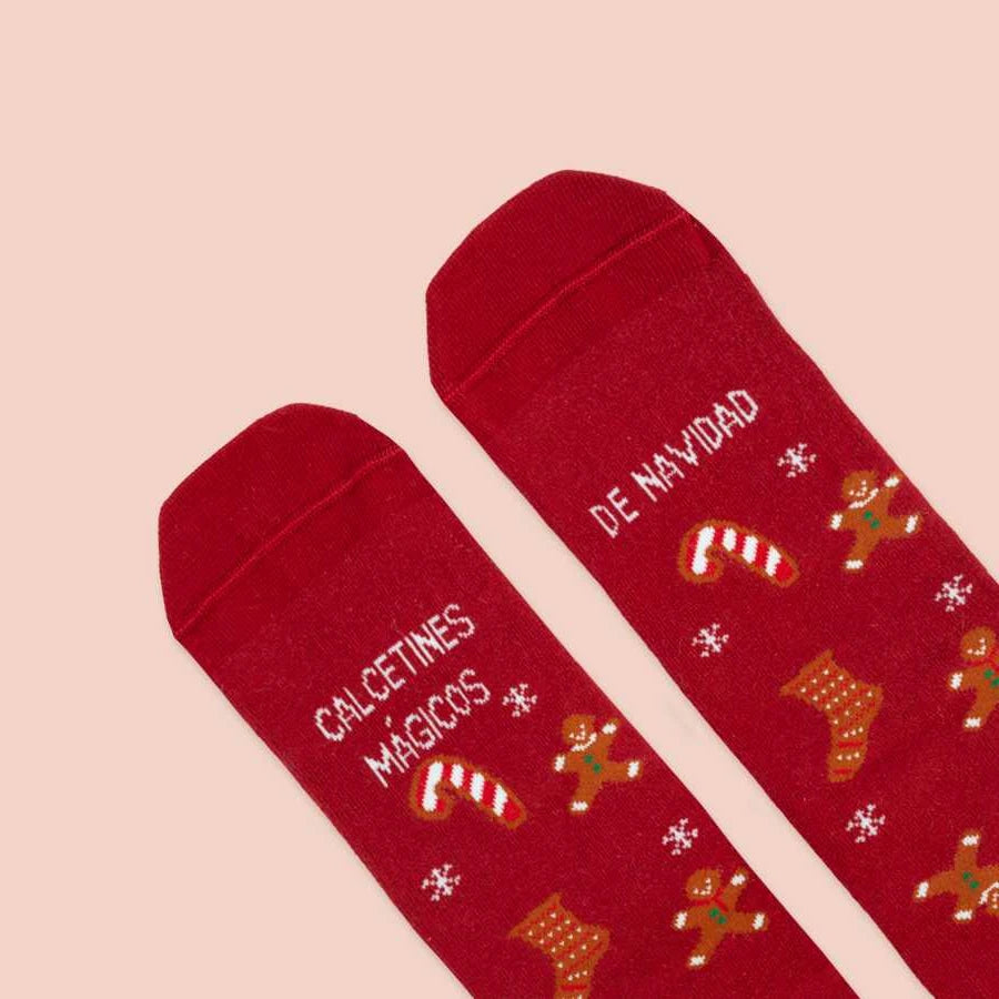 Detalle de la punta de los calcetines de navidad rojos y verdes con estampado de calcetines, galletas de jengibre, árboles, copos y bastones de caramelo y el mensaje "Calcetines Mágicos de Navidad"