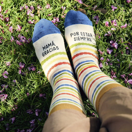 Pies sobre la hierba con los calcetines a rayas de colores y puntera azul con el mensaje "Mamá gracias por estar siempre"