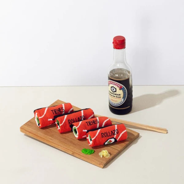 Tabla con los calcetines Tienes Rollazo de UO con los colores del sushi enrollados junto a wasabi y un bote de salsa de soja