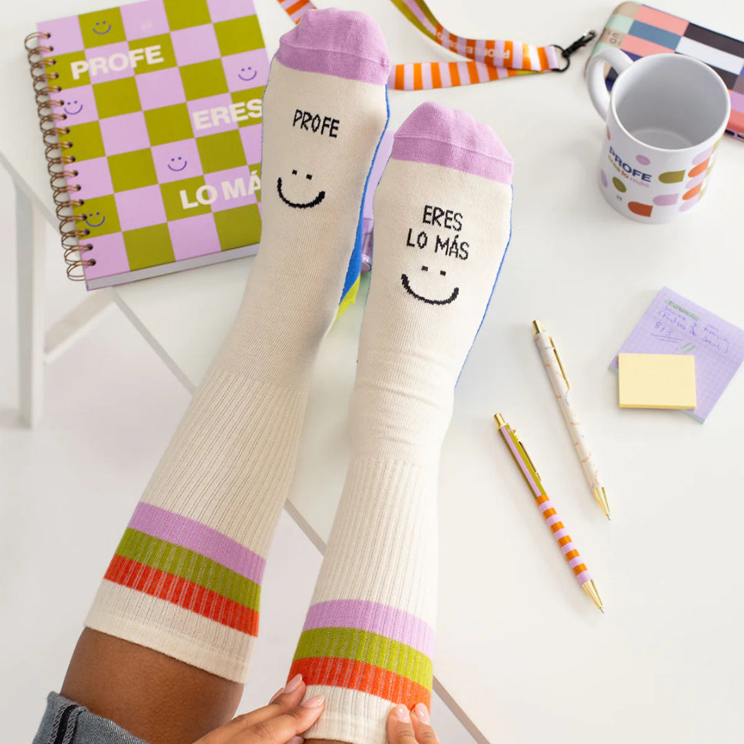 Pies apoyados en un escritorio con los calcetines de Profe eres lo más en color beige con la puntera lila
