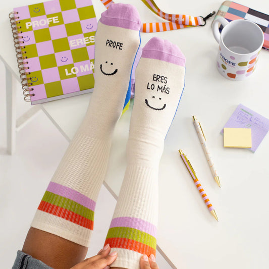 Pies apoyados en un escritorio con los calcetines de Profe eres lo más en color beige con la puntera lila