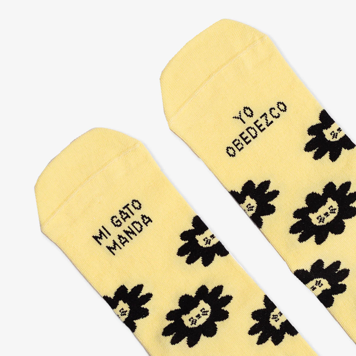 Detalle de la puntera de los calcetines amarillos con estampado de caras de gato y el mensaje "Mi gato manda / yo obedezco"