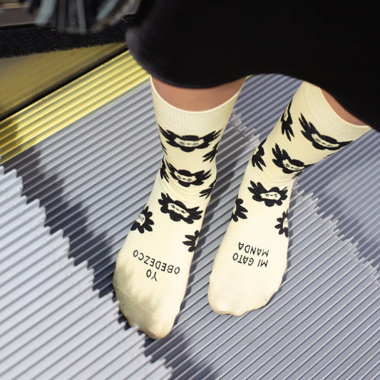 Persona descalza en una escalera mecánica con los calcetines amarillos con estampado de caras de gato y el mensaje "Mi gato manda / yo obedezco"