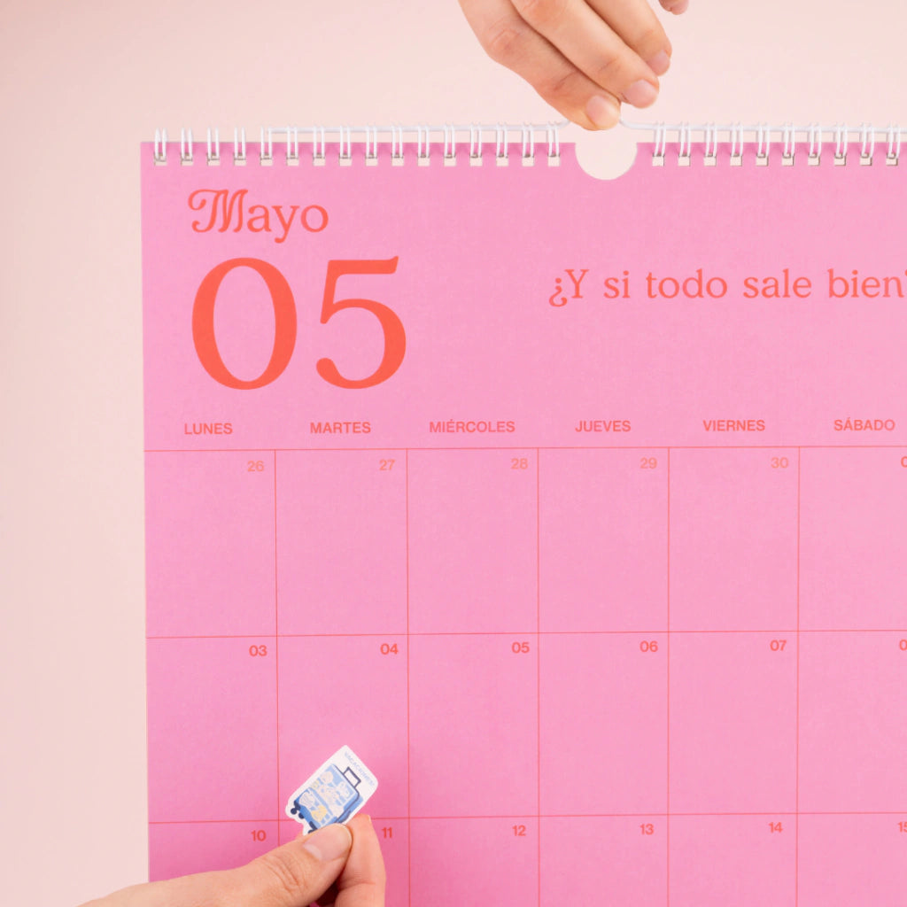 Detalle del mes de mayo del calendario de pared 2027 de la artista argentina Happimess con frases motivadoras, espacio para escribir y una mano colocando una de las pegatinas incluidas