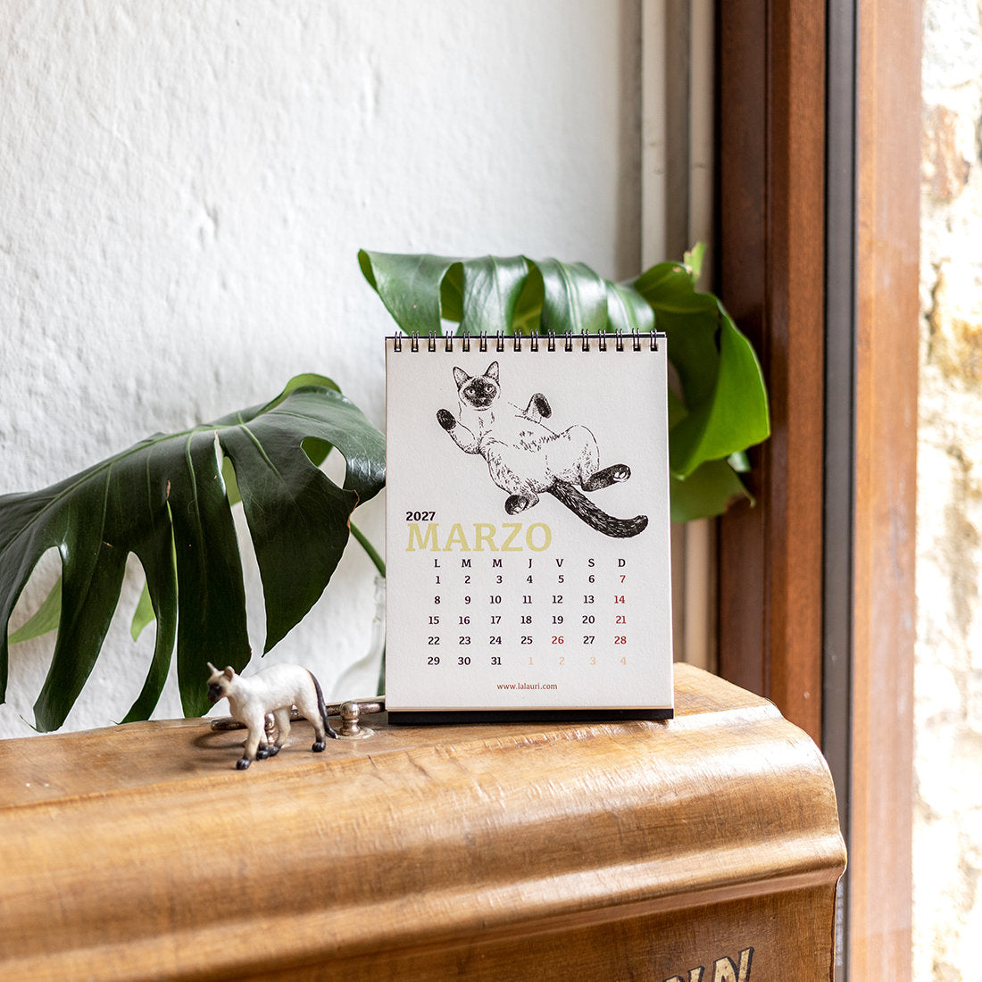 Calendario de escritorio ilustrado de Laura Agustí sobre un mueble de madera con el mes de marzo con ilustración de un gato siamés panzarriba