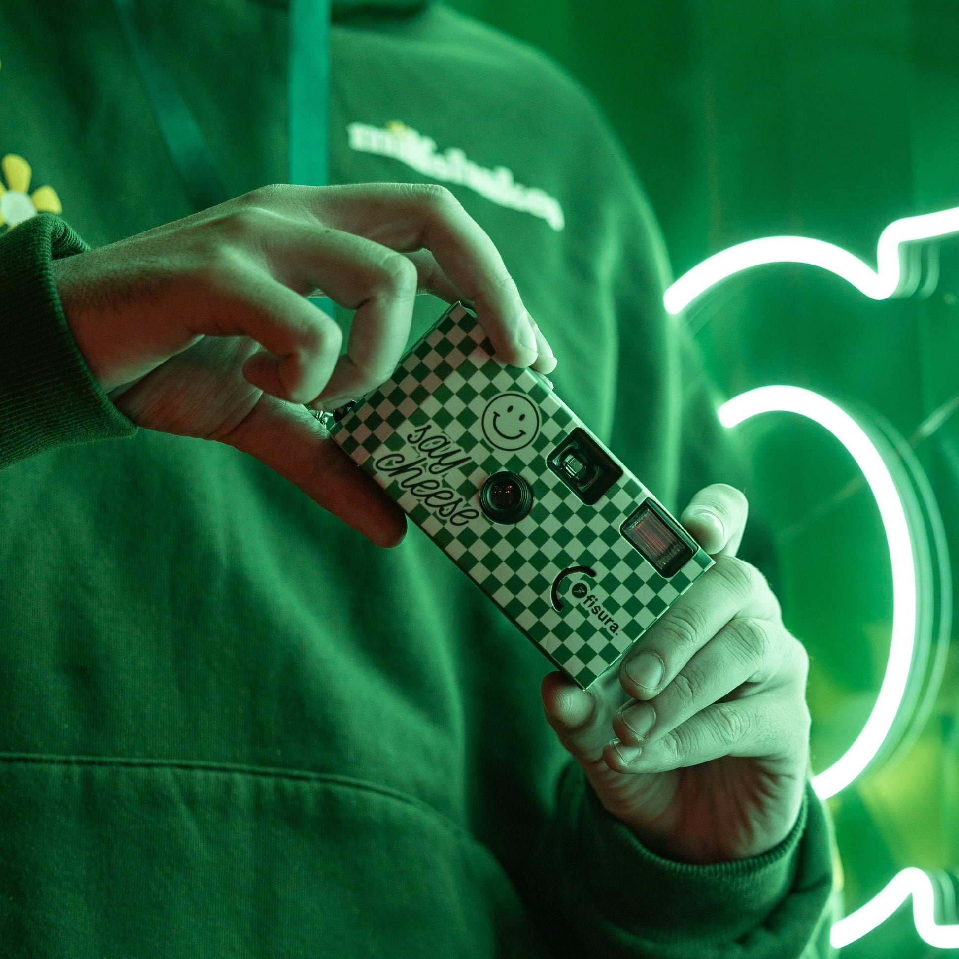 Joven con sudadera, una cámara desechable y luces de neon al fondo