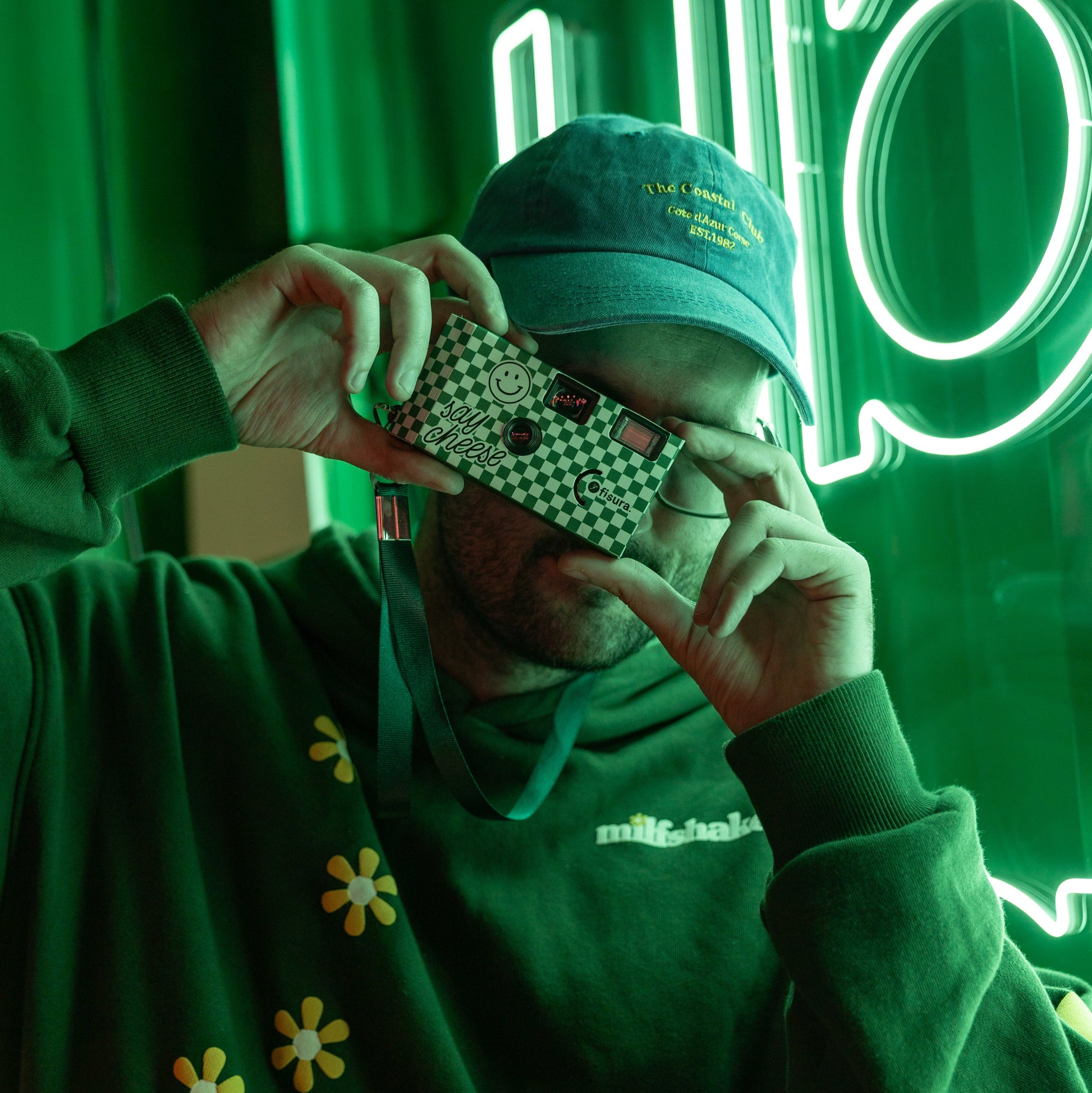 Chico con sudadera y gorra verdes haciendo una foto con cámara desechable