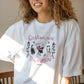 modelo con la camiseta en color blanco de la ilustradora maria gomez y la marca voraz con el texto Gatos, libros y vino será mi destino y un dibujo de una chica leyendo tumbada en la hierba con una copa de vino y dos gatos a su lado