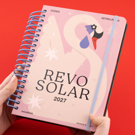 Portada de la Agenda Astrológica 2027 Cisne Revo Solar de Dominio Salvaje con tapa rosa, ilustración de cisne estilizado, espiral azul y elástico de cierre, sostenida por dos manos sobre fondo rojo