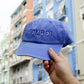 Gorra azul con la palabra Cmboi frente a fachadas modernistas del barrio de Ruzafa