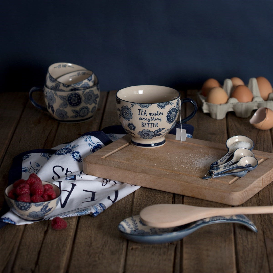 Cucharas de medir de la colecciónSauce Azul con estampado florar alrededor de otros objetos de cocina de la misma colección en un fondo gastronómico 