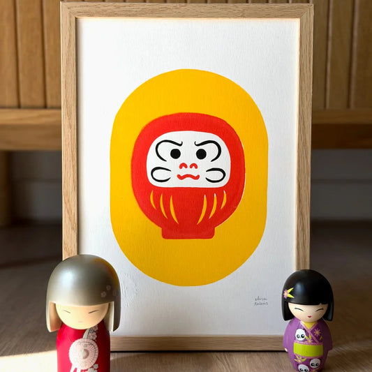 Serigrafía de estilo japonés con un Daruma rojo sobre fondo amarillo. Al pie, muñecas japonesas