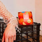 caja de calcetines en forma de caja del supermercado con dos pares de calcetines presentados en forma de naranjas, sobre una caja de naranjas y un modelo apoyando el brazo