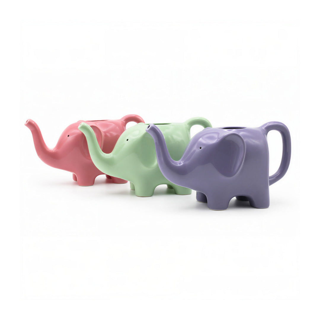 Tres regaderas en forma de elefante en colores rosa, verde y lila encima de un fondo blanco. 